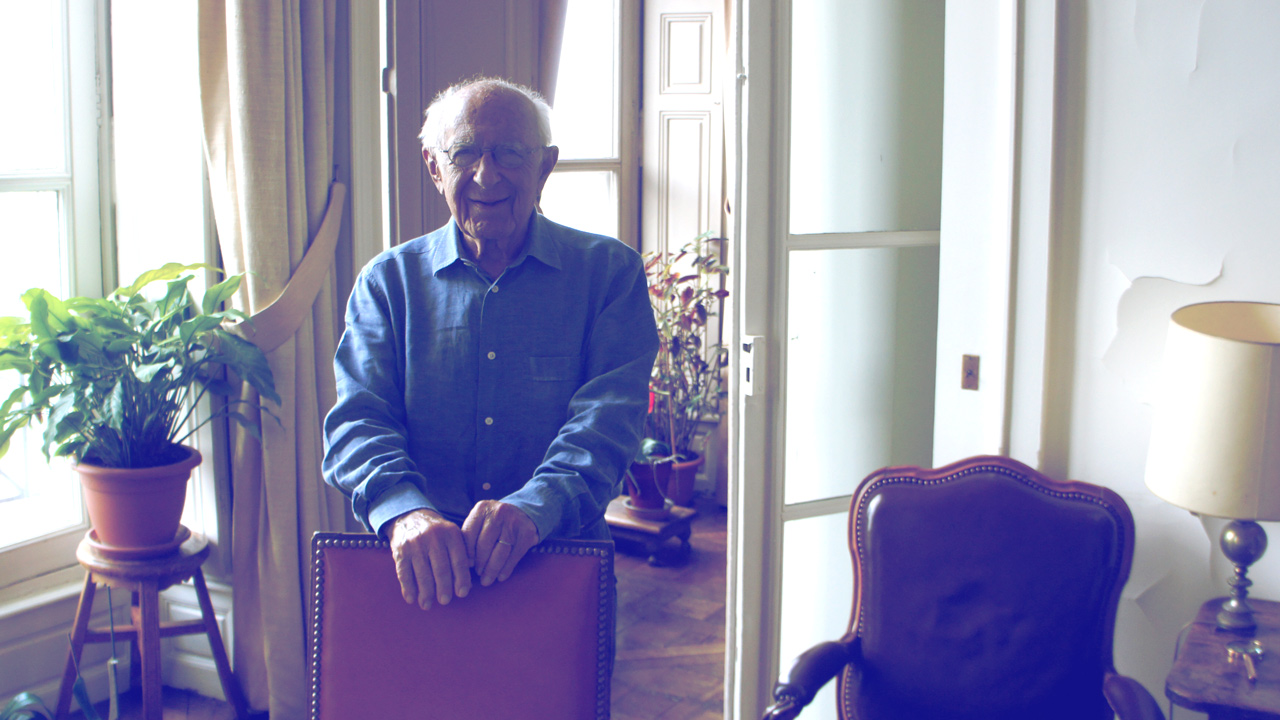 Claude Alaphandéry dans son salon, debout derrière un fauteuil